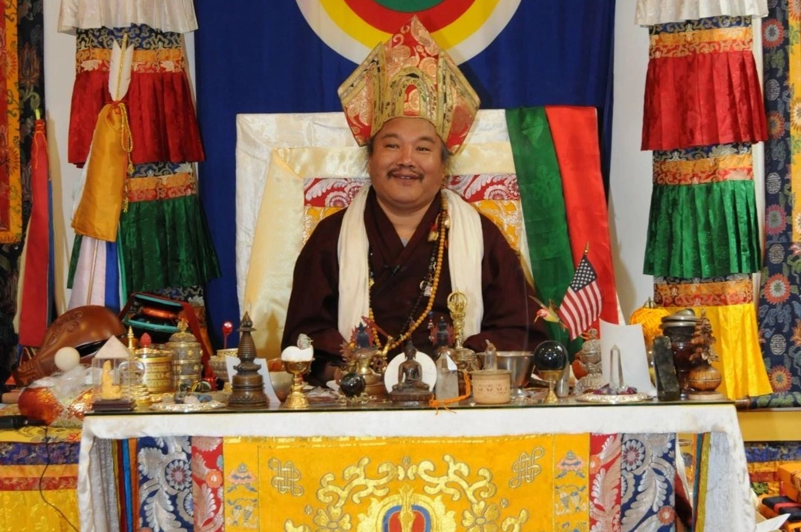Dzogchen Khenpo Choga Rinpoche in traditional robes seated before a shrine