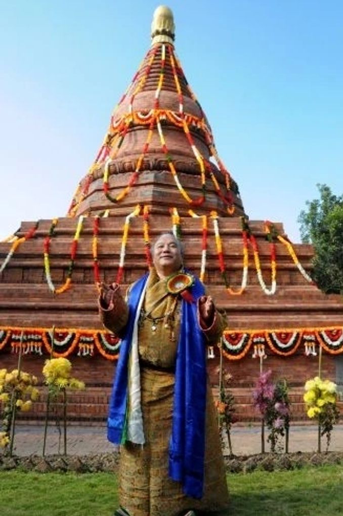 A person in traditional attire stands before a decorated stupa.